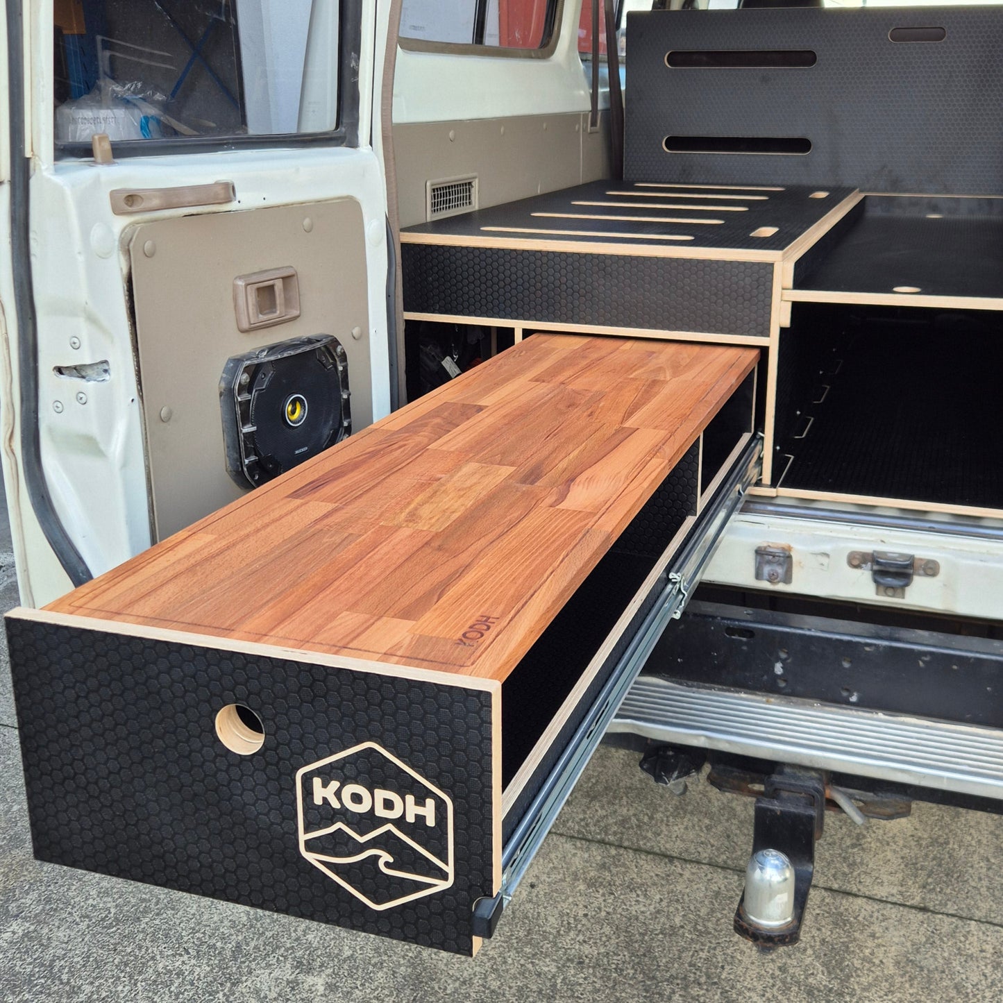 Wooden storage unit with 'KODH' branding attached to a vehicle.